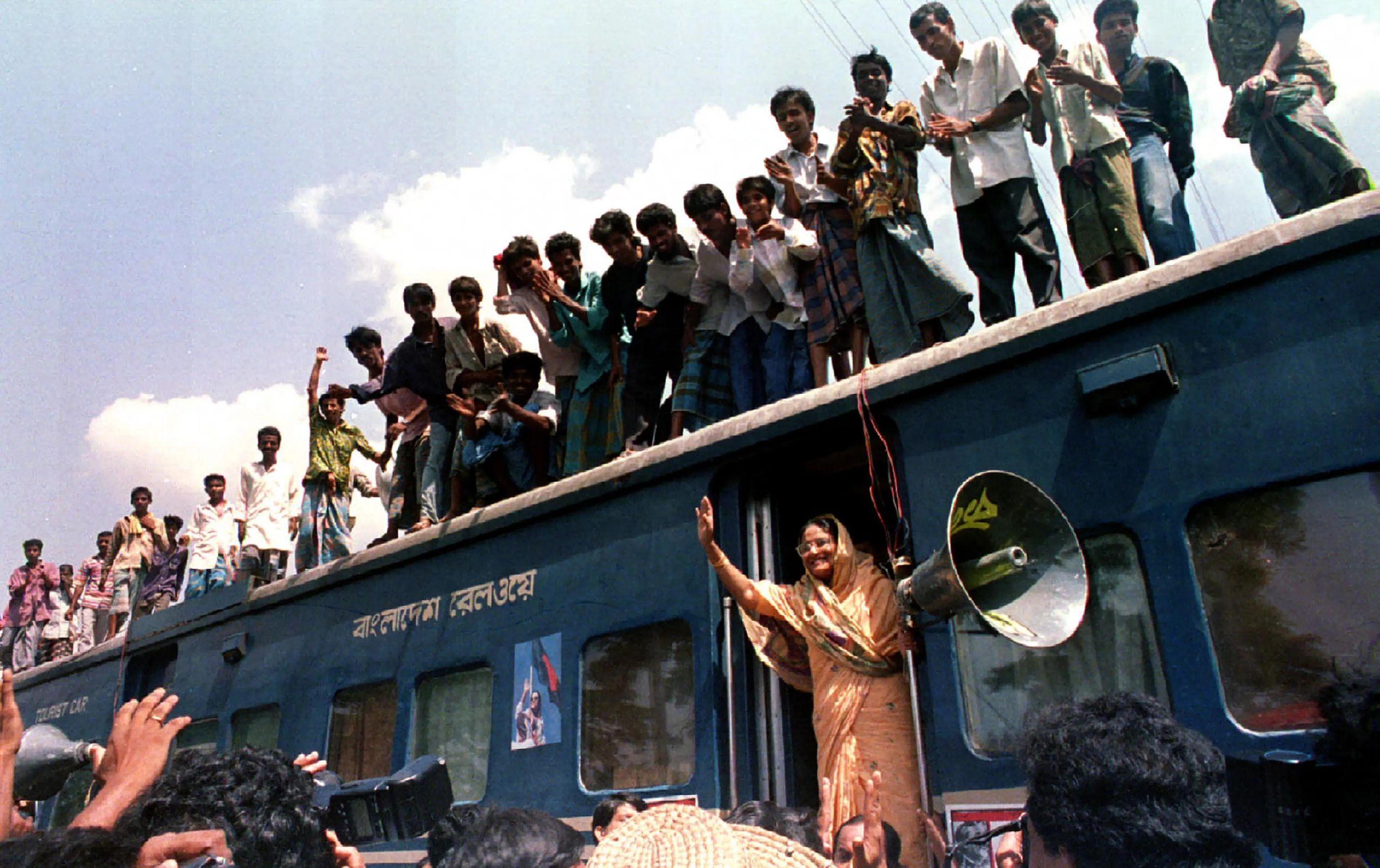Sheikh Hasina waving from the door of a railway carriage, with a crowd cheering on its roof